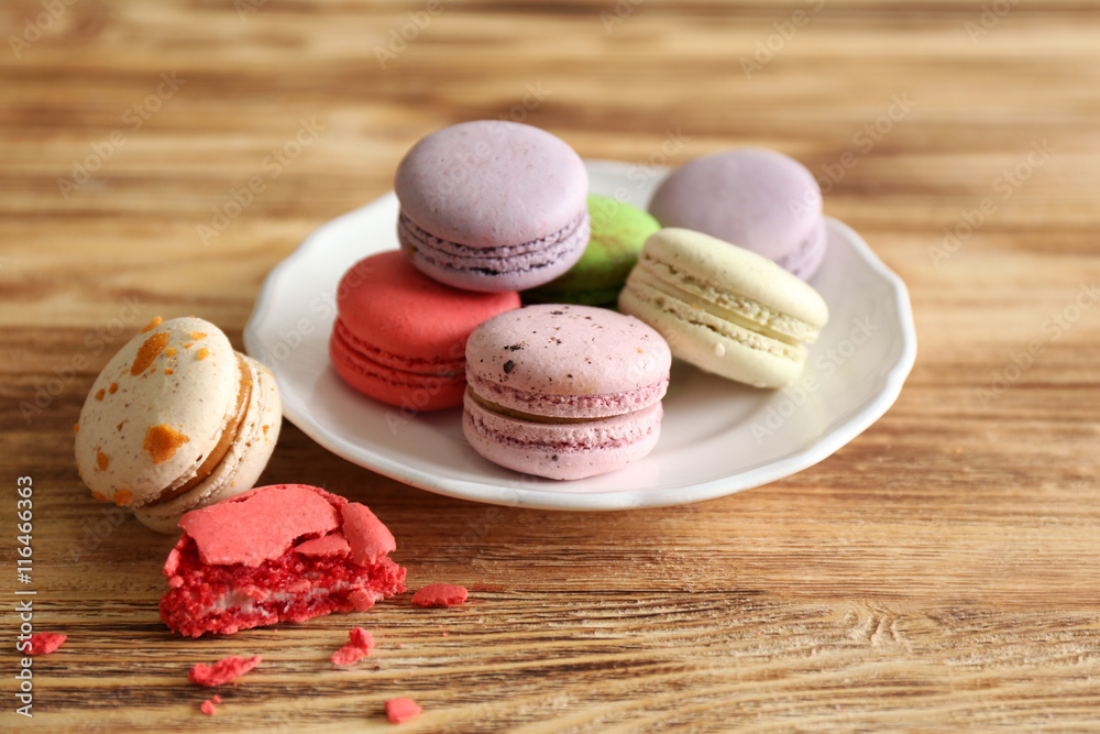 Colorful tasty macaroons in plate on wooden background