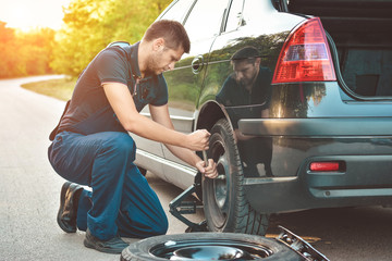 Auto mechanic changing  tire on car on road