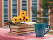 Чай в большой кружке, стопа книг и букет  цветов на балконе на фоне окон. 