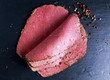© grinchh - Peppered roast beef pastrami slices on paper with grains of coloured pepper.