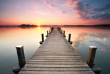 Fototapeta Pomosty - langer Holzsteg am Seeufer zum Sonnenaufgang im Sommer