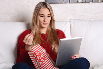 Young woman eating popcorn and watching movies on tablet.