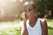 © wayhome.studio  - Close up portrait of dark skinned female laughing at a joke while having a phone conversation, enjoying summer sunny day in the city park, wearing stylish sunglasses, looking carefree and happy