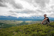 © rammellzee - male traveler  sitting on the grass on a background of mountains