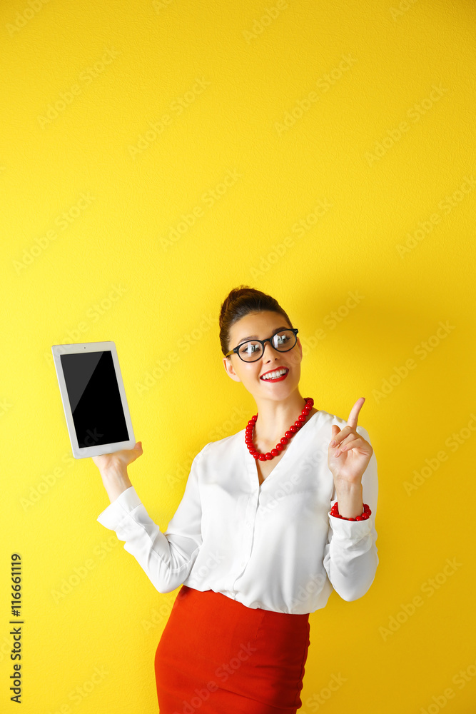 Pretty young woman holding tablet on yellow background