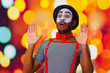 Headshot pantomime man with facial paint posing for camera using hands interacting, blurry lights background