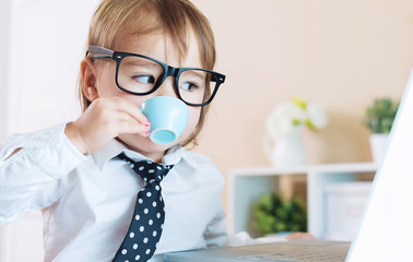 Wall Mural - Smart toddler girl with glasses drinking coffee while using a laptop