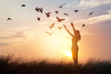 woman praying and free birds enjoying nature on sunset background