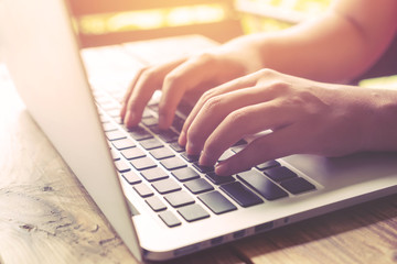 Side view shot of beautiful young hipster woman's hands busy working on her laptop sitting at wooden table in a coffee shop - retro filter effect and vintage color style