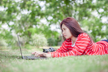 Portrait of happy young woman lying on grass and using laptop co