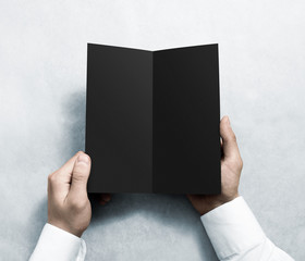 Fototapete - Hand opening blank black flyer brochure booklet mockup. Leaflet presentation. Pamphlet mock up holding hand. Man show grey offset paper. Booklet design template. Paper sheet display read first person
