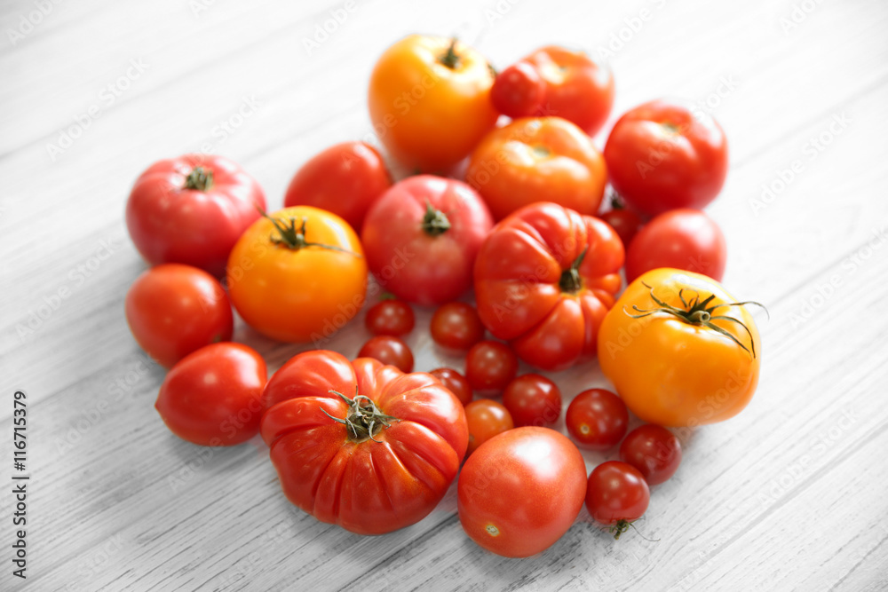 Heart shape of different tomatoes on light wooden background