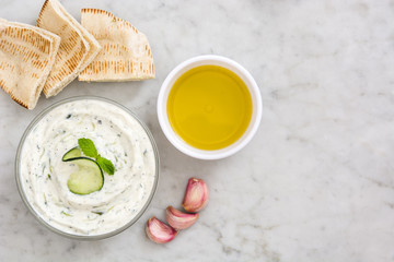 Tzatziki in bowl and ingredients on white marble
