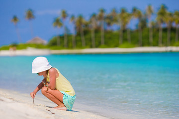 Wall Mural - Adorable little girl at beach during summer vacation drawing on sand