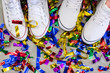 Two feet in white shoes between multicolored festive confetti on the grey floor