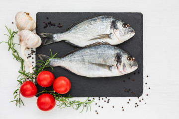 Fresh dorado fish on slate cutting board with rosemary, garlic and tomatoes. Top view, copy space 