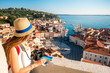 Young female traveler with red backpack and hat enjoying the view from George's tower on Piran old town. Traveling in Slovenia