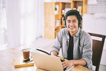 Asian student in headphones working on laptop at home