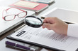 © thbangkok - Businessman or HR Manager review a resume on his desk with Magnifier, computer laptop, digital tablet, calculator and glasses. Resume information with magnifier.
