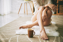 Legs Of Woman Sitting On The Floor With Cup Of Coffee