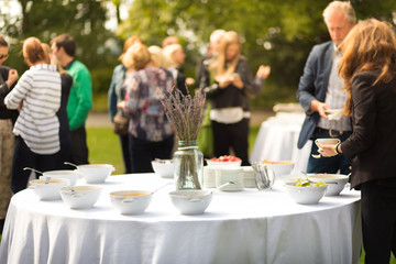 Banquet lunch break at conference meeting on hotel terrace. Assortment of food and beverage. Unrecognizable people discussing over food in background.