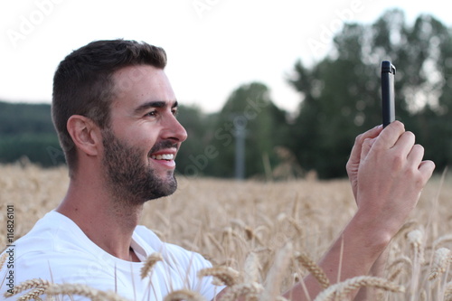 Juliste Young smiley man playing a video game in remote wheat field