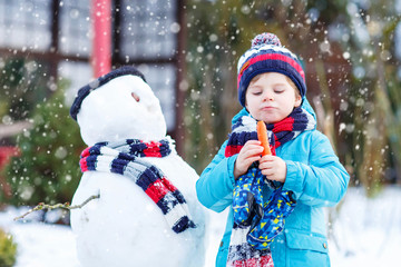 Poster - Funny kid boy making a snowman in winter outdoors