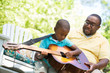 © digitalskillet1 - African American man teaching his son how to play the guitar