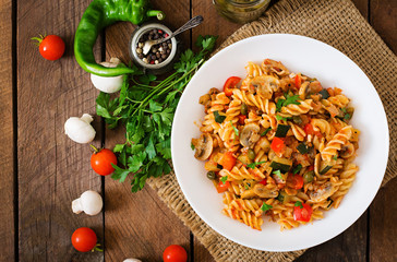 Wall Mural - Vegetarian Vegetable pasta Fusilli with zucchini, mushrooms and capers in white bowl on wooden table. Top view