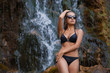 Beautiful young girl in bathing suit standing at the foot of the waterfall