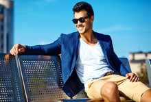High Fashion Look.Young Stylish Confident Happy Handsome Businessman Model Man In Blue Suit Clothes In The Street Sitting On A Bench