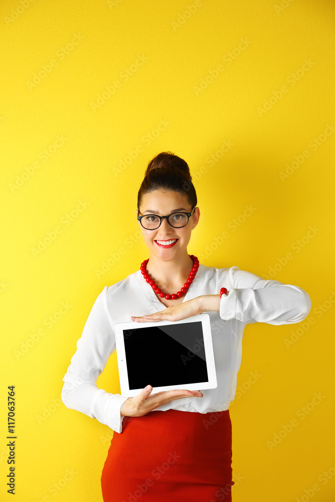 Pretty young woman holding tablet on yellow background