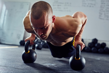 Wall Mural - Closeup of athletic man doing kettlebell pushups at the gym