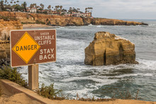Close-up View Of Danger Sign With Bird Rock In Background At Sunset Cliffs In San Diego, California.   