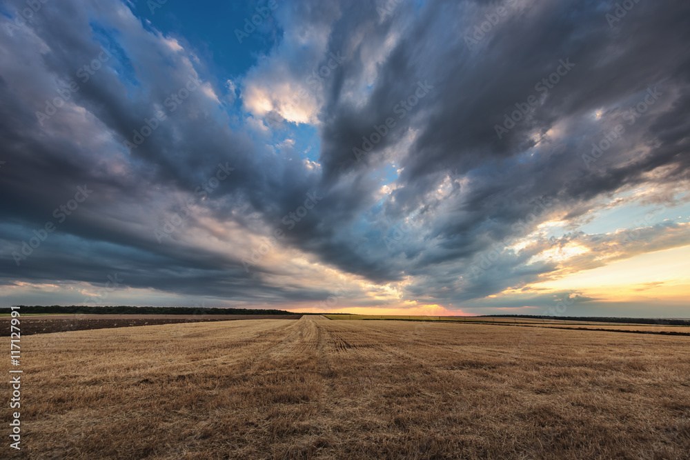 Dramatic clouds over the field after harvest - obrazy, fototapety, plakaty 