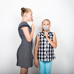 Two cute little girlfriend eating bright lollipops. Funny kids. Best friends pamper and posing