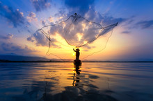 Asian Fisherman On Wooden Boat Casting A Net For Catching Freshwater Fish In Nature River In The Early Morning Before Sunrise