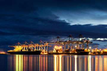 Wall Mural - Container Cargo freight ship with working crane bridge in shipyard at dusk for Logistic Import Export background