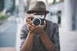 Half length of young beautiful afro black man outdoor in the city holding instant camera, shooting - photography, creative, artist concept