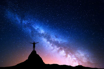 night landscape with milky way. silhouette of a standing man with raised up arms on the top of mount