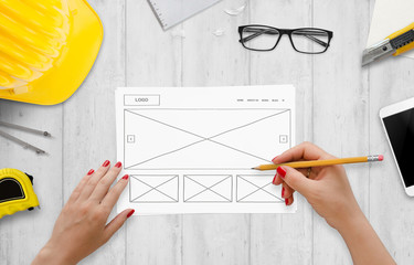 Leinwandbilder - Drawing website idea on paper. Work desk with smart phone, glasses, paper, pencil, construction tools.