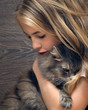Young beautiful girl with long blond hair tenderly hugging gray fluffy cat