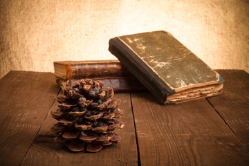 Still life - A stack of old books and pine cone on old wooden ta