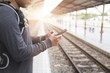 man holding smartphone with backpack at train station