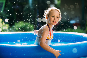 Portrait of cute little girl in blue big inflatable pool outdoors