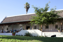 Exterior View Of A Farm House With Thatch Roof And Large Patio. 