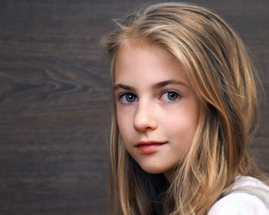 Portrait of a teen girl. Long blond hair, a pretty face. Background dark wooden board