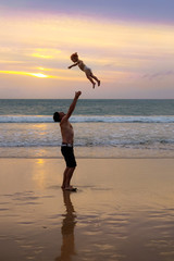 Father throws his daugter at the beach near the sea at the spect