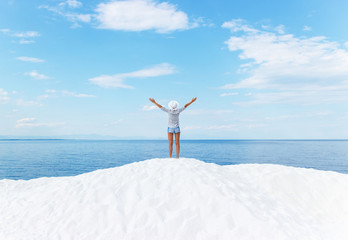 Young woman standing on white beach with her arms outstretched. She is looking towards the horizon.