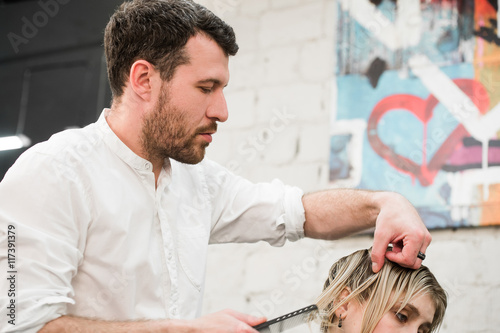 Male hairdresser making haircut for a client in professional hairdressing salon Slika na platnu